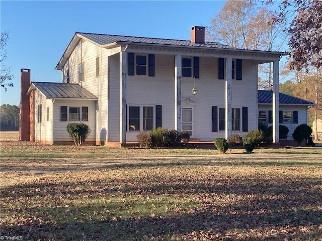 back of house with a chimney, metal roof, and a yard