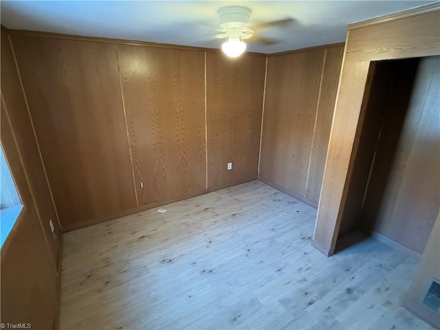 unfurnished bedroom featuring ceiling fan, wood walls, and light wood-type flooring