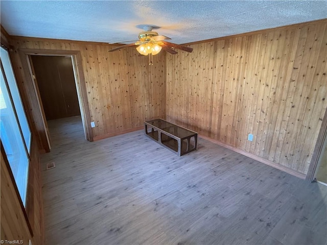 spare room with wood walls, ceiling fan, wood-type flooring, and a textured ceiling