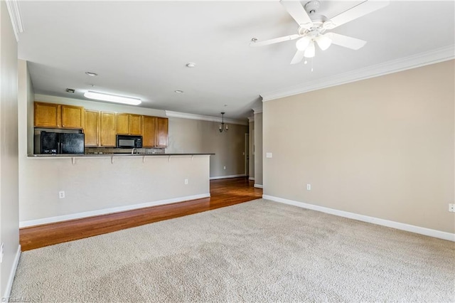 kitchen with brown cabinets, black appliances, dark countertops, crown molding, and baseboards