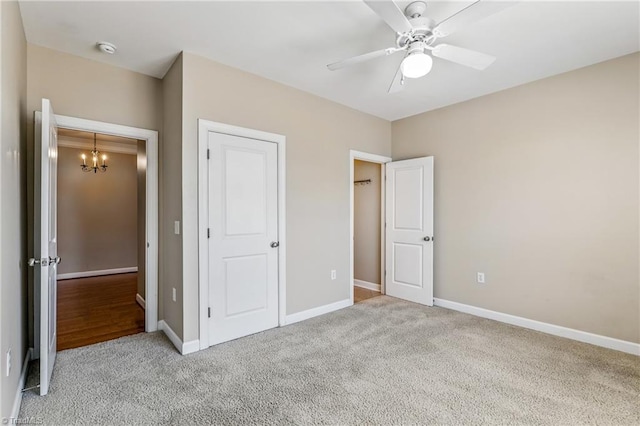 unfurnished bedroom with light carpet, ceiling fan with notable chandelier, and baseboards