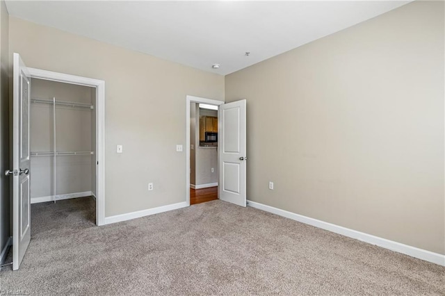 unfurnished bedroom featuring a closet, light colored carpet, a walk in closet, and baseboards