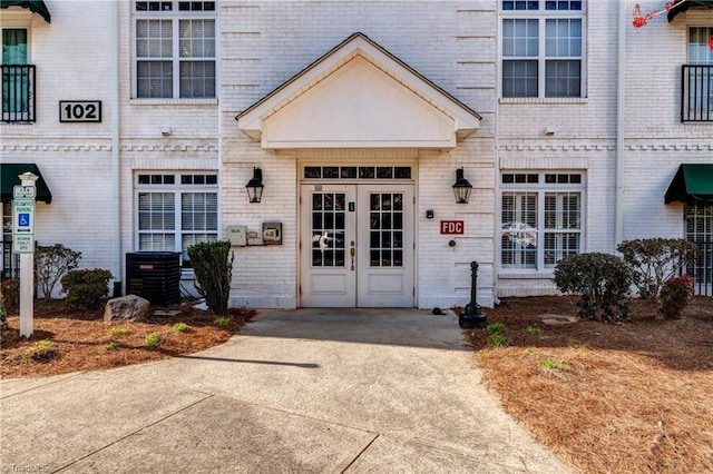 view of exterior entry featuring brick siding, central AC unit, and french doors