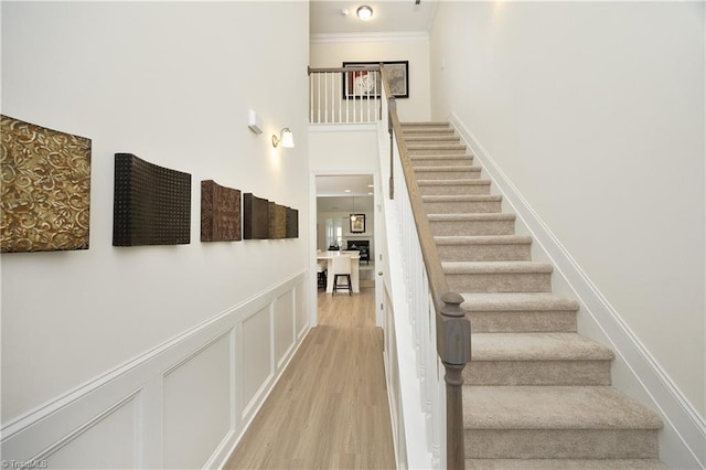 staircase featuring crown molding, wood-type flooring, and a towering ceiling