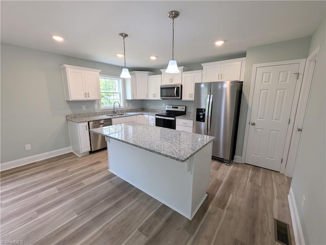 kitchen featuring pendant lighting, stainless steel appliances, light stone counters, white cabinets, and a kitchen island