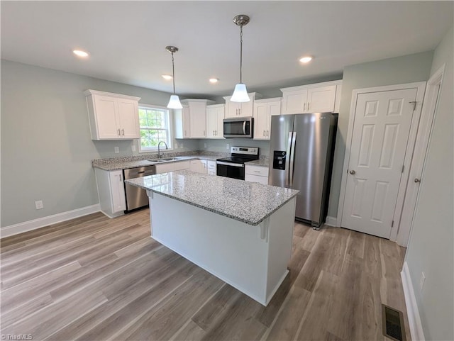 kitchen with visible vents, stainless steel appliances, white cabinetry, light wood-type flooring, and a center island