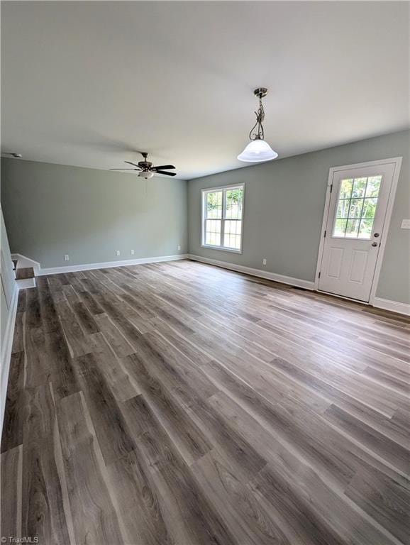 unfurnished living room featuring dark wood-style floors, ceiling fan, and baseboards