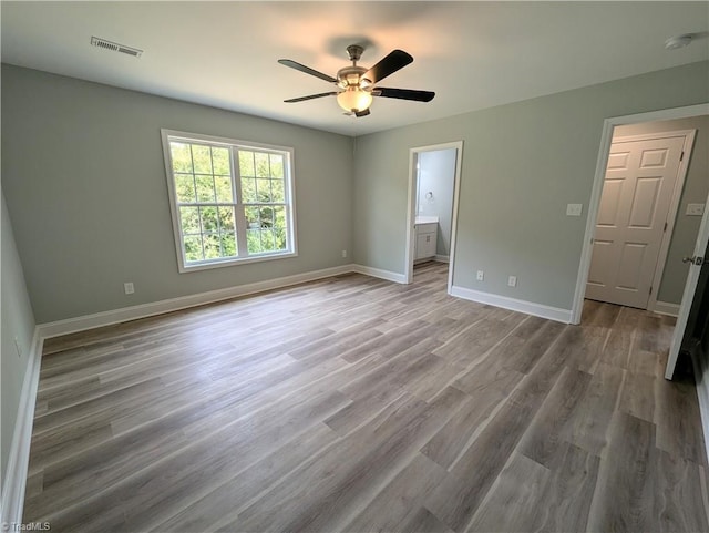 unfurnished bedroom with wood finished floors, baseboards, visible vents, and connected bathroom