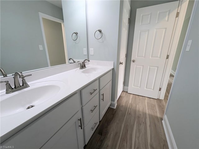 full bathroom featuring double vanity, wood finished floors, baseboards, and a sink