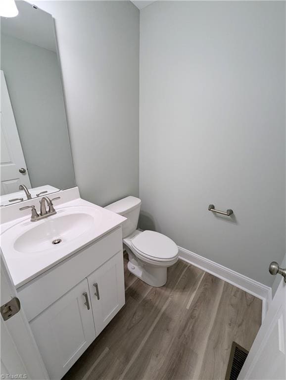 half bathroom featuring visible vents, baseboards, toilet, wood finished floors, and vanity
