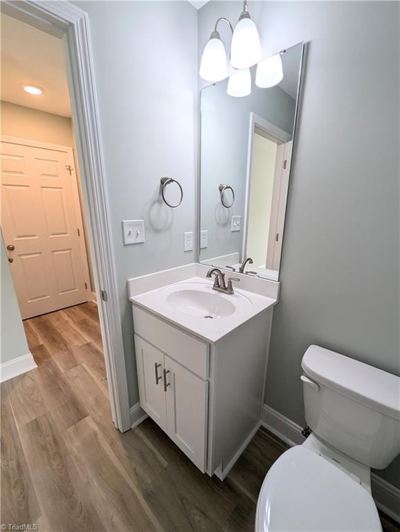 half bathroom with baseboards, a chandelier, toilet, wood finished floors, and vanity