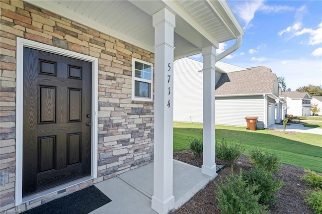 view of exterior entry featuring a porch, stone siding, and a yard