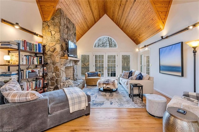 living room featuring a stone fireplace, high vaulted ceiling, wooden ceiling, light wood-type flooring, and french doors