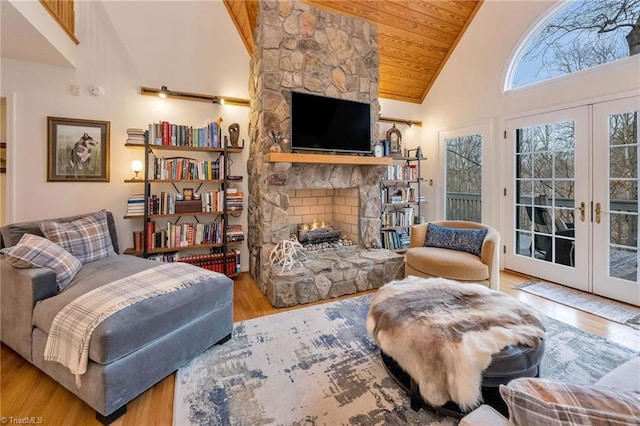 living room featuring a stone fireplace, high vaulted ceiling, wooden ceiling, light wood-type flooring, and french doors