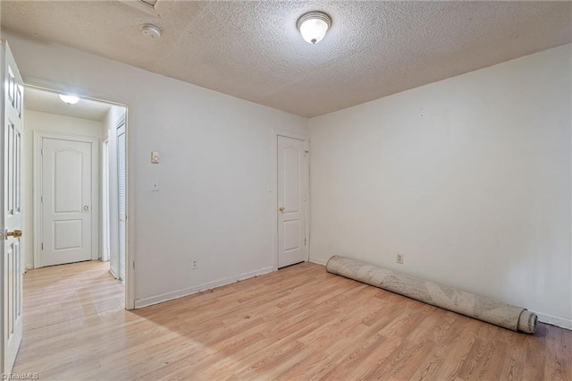 spare room featuring light wood finished floors, a textured ceiling, and baseboards