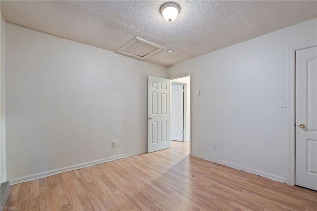 unfurnished room featuring baseboards, a textured ceiling, attic access, and light wood-style flooring