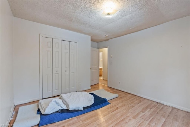 bedroom with a closet, a textured ceiling, baseboards, and wood finished floors