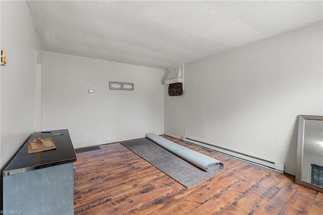 bedroom with a textured ceiling, a baseboard heating unit, and wood finished floors