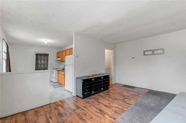 kitchen featuring visible vents, light wood-style floors, brown cabinetry, white appliances, and a textured ceiling