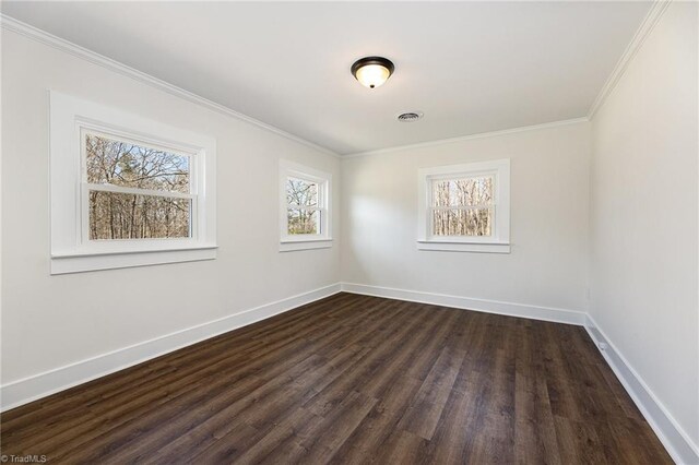 empty room featuring visible vents, dark wood-type flooring, baseboards, and ornamental molding