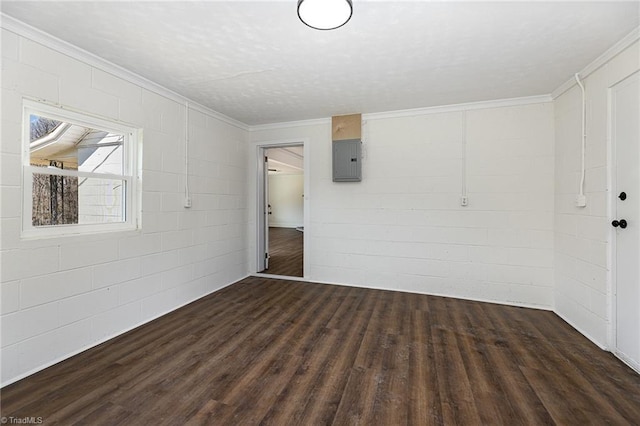 empty room featuring electric panel, ornamental molding, concrete block wall, and dark wood-style flooring