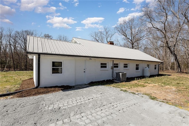 view of front of property with concrete block siding, a chimney, central AC, and metal roof