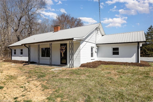 view of front of house featuring a chimney, concrete block siding, a front lawn, and metal roof