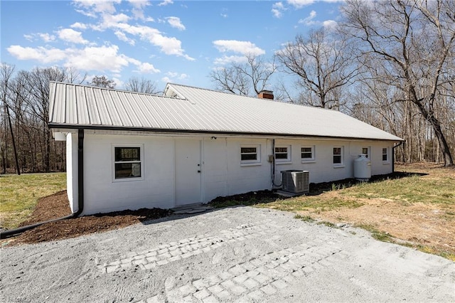 view of front of home with a chimney, concrete block siding, central AC, and metal roof