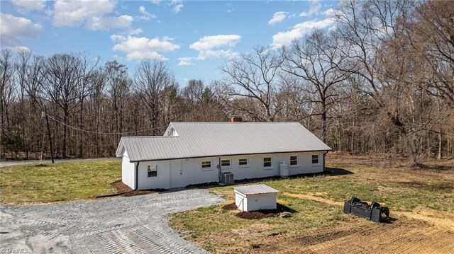 exterior space with gravel driveway, a yard, central AC, and metal roof