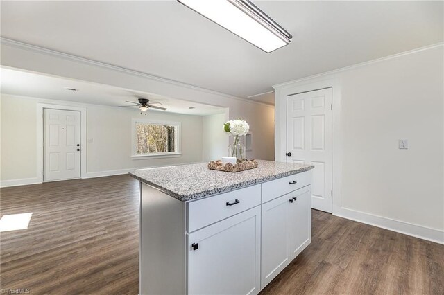 kitchen featuring dark wood-type flooring, ornamental molding, a center island, baseboards, and light stone countertops