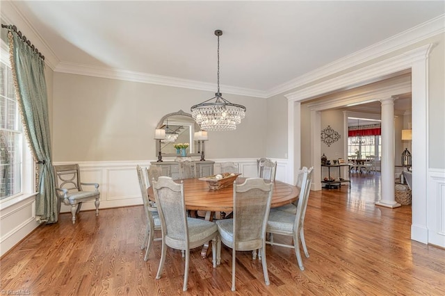 dining area with crown molding, a notable chandelier, light hardwood / wood-style flooring, and ornate columns