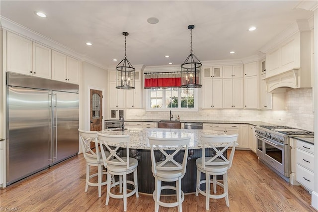 kitchen with hanging light fixtures, a center island with sink, premium appliances, light stone countertops, and white cabinets