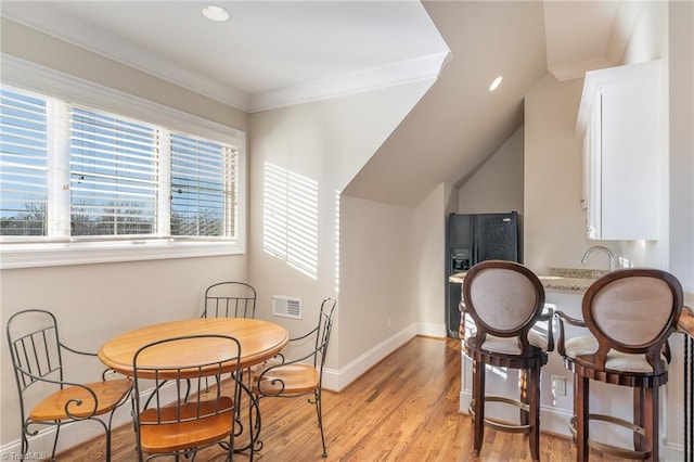 dining area with lofted ceiling, ornamental molding, and light wood-type flooring