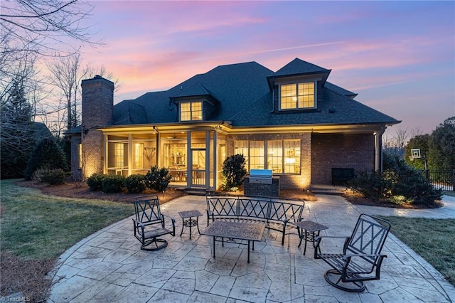 back house at dusk with a yard, exterior kitchen, and a patio