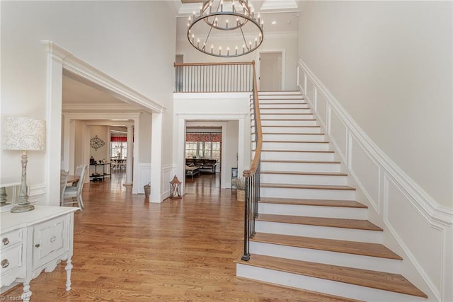 stairs with hardwood / wood-style flooring, crown molding, a towering ceiling, and a chandelier