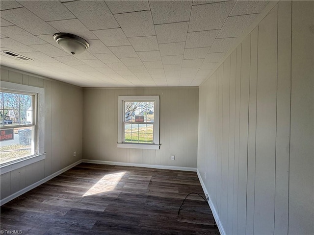 empty room with a wealth of natural light, wooden walls, and dark wood-type flooring