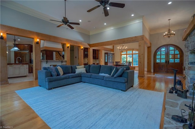 living room with light hardwood / wood-style floors, ceiling fan with notable chandelier, crown molding, a towering ceiling, and sink