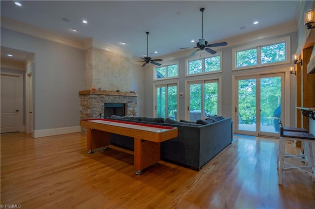 game room featuring ceiling fan, a stone fireplace, hardwood / wood-style floors, and a healthy amount of sunlight