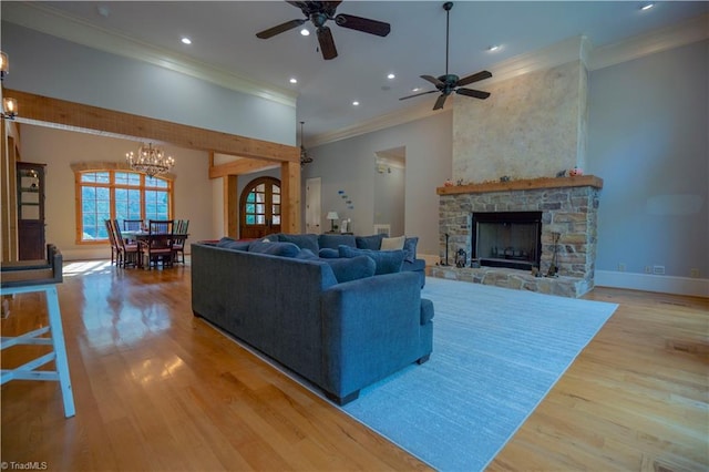 living room featuring ceiling fan with notable chandelier, light hardwood / wood-style flooring, a fireplace, and ornamental molding