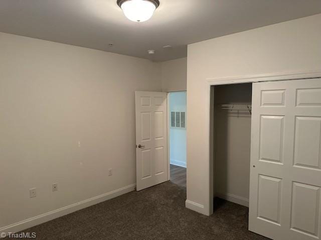 unfurnished bedroom with a closet, dark carpet, visible vents, and baseboards