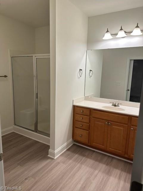 bathroom featuring a stall shower, wood finished floors, vanity, and baseboards