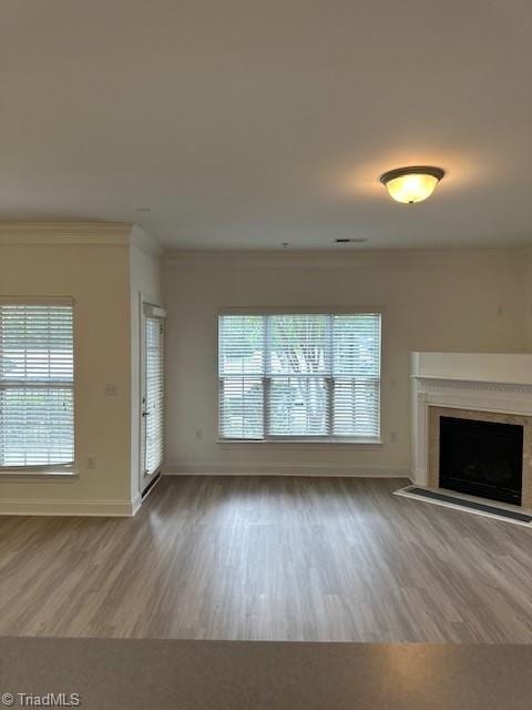 unfurnished living room with baseboards, wood finished floors, a fireplace with flush hearth, and crown molding