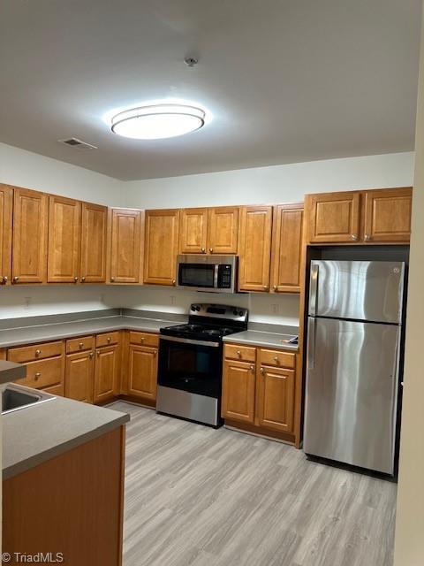 kitchen with appliances with stainless steel finishes, brown cabinets, light wood-style floors, and visible vents