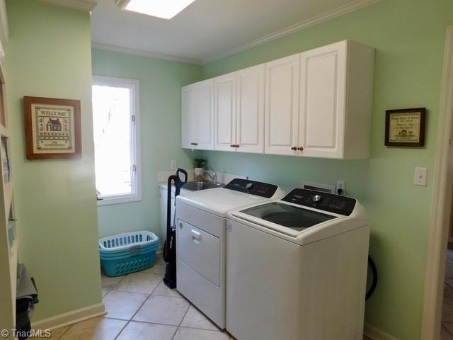 clothes washing area with crown molding, cabinets, washer and clothes dryer, and light tile patterned floors