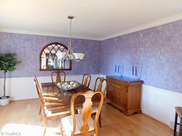 dining room with an inviting chandelier, ornamental molding, and light wood-type flooring