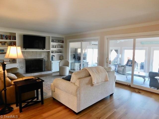 living room featuring built in features, hardwood / wood-style floors, a fireplace, ornamental molding, and an AC wall unit