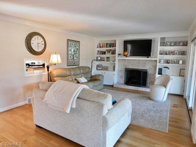 living room featuring light hardwood / wood-style flooring, crown molding, and a fireplace