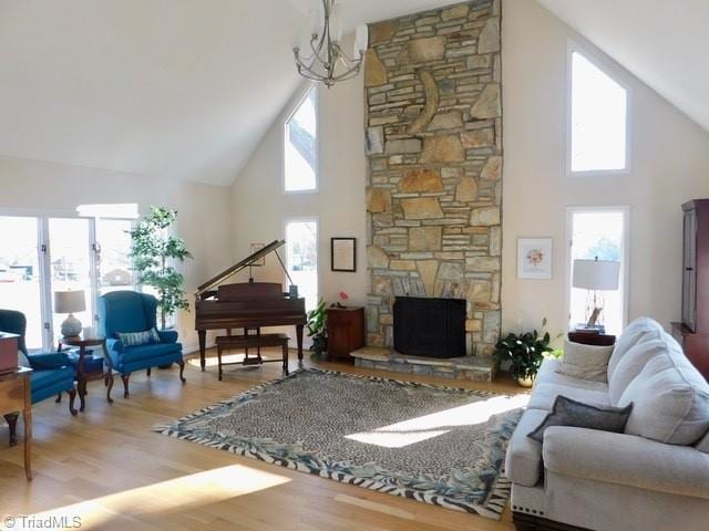 living room with plenty of natural light, a stone fireplace, high vaulted ceiling, and light hardwood / wood-style flooring