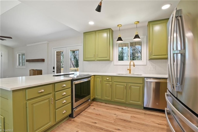 kitchen with a ceiling fan, a peninsula, a sink, stainless steel appliances, and green cabinets