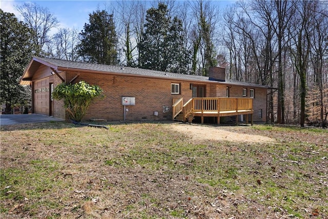 back of property featuring a deck, driveway, an attached garage, brick siding, and a chimney